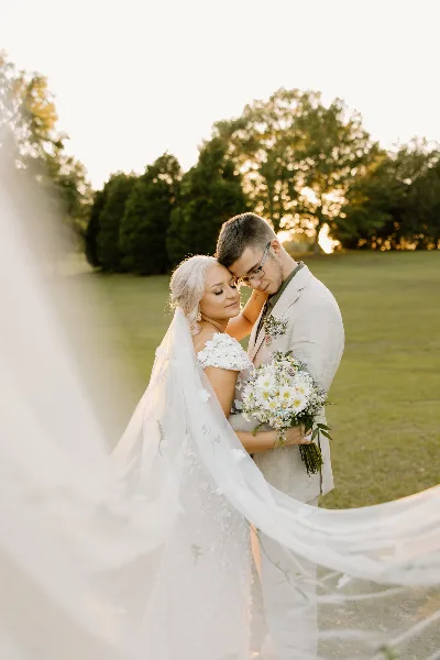 A bride and groom embracing outdoors with a bouquet and veil.