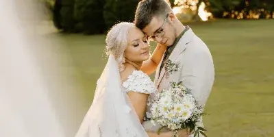 A bride and groom embracing outdoors with a bouquet and veil.
