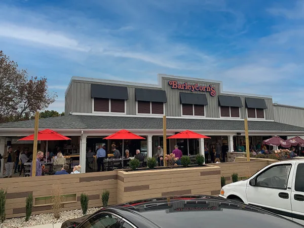 Exterior view of a Barleycorn's restaurant with red patio umbrellas and outdoor seating.