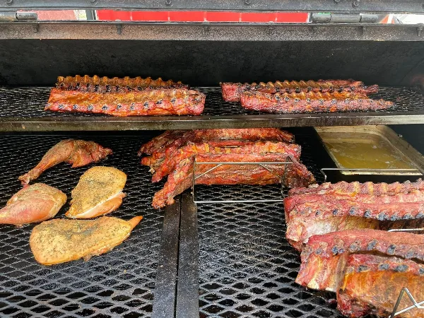 A commercial smoker containing racks of ribs, brisket, and seasoned poultry.