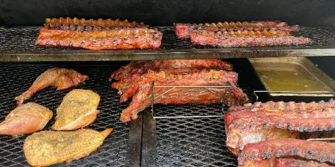 A commercial smoker containing racks of ribs, brisket, and seasoned poultry.