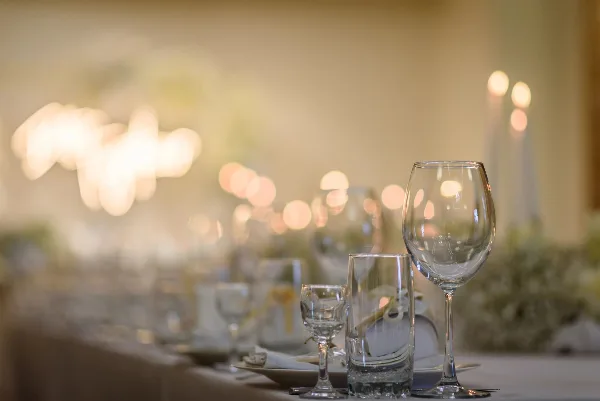 A close-up view of a set event table featuring wine glasses, water glasses, and plates with a warm, bokeh-lit background.