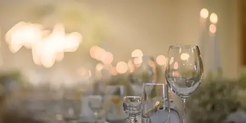 A close-up view of a set event table featuring wine glasses, water glasses, and plates with a warm, bokeh-lit background.
