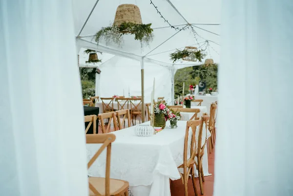 White event tent interior with draped fabric, wooden chairs, and tables set with white linens and floral centerpieces.