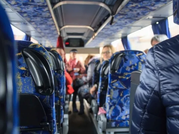 Interior view of a passenger bus with blue patterned seats and passengers boarding.