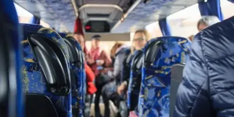 Interior view of a passenger bus with blue patterned seats and passengers boarding.