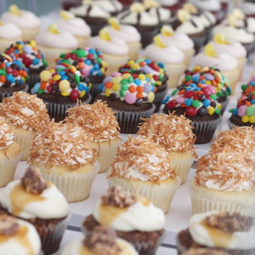 A display of various decorated cupcakes topped with sprinkles, coconut, and frosting.