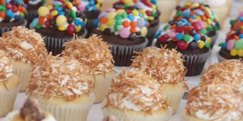 A display of various decorated cupcakes topped with sprinkles, coconut, and frosting.