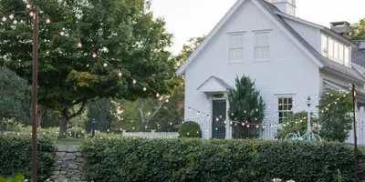 Outdoor wedding reception setup featuring string lights, floral centerpieces, and a white building in the background.
