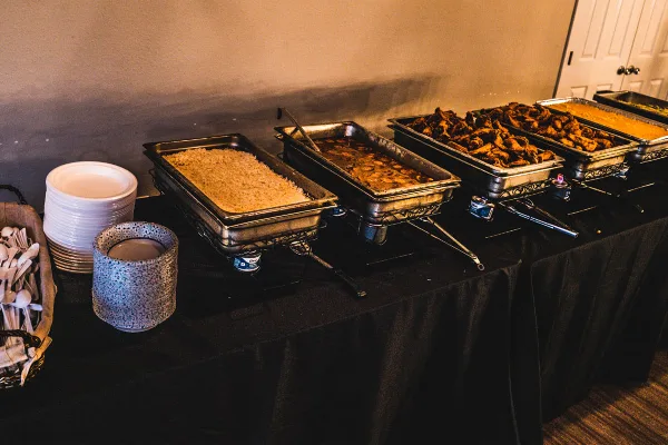 A catering buffet table featuring multiple chafing dishes filled with rice, meat, and other food items.