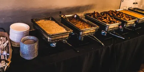 A catering buffet table featuring multiple chafing dishes filled with rice, meat, and other food items.