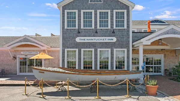 Exterior view of The Nantucket Inn building featuring a gray shingled facade, white-trimmed windows, and a wooden boat display in the foreground.