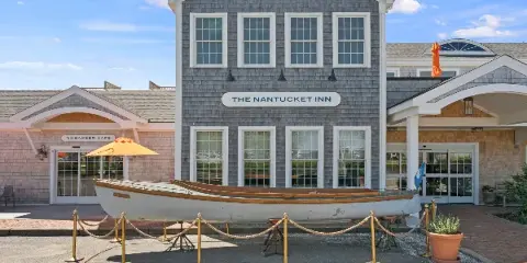 Exterior view of The Nantucket Inn building featuring a gray shingled facade, white-trimmed windows, and a wooden boat display in the foreground.