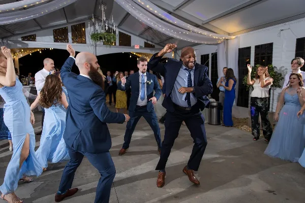 Guests dancing on a wedding dance floor under a tent with string lights.