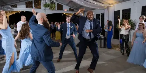 Guests dancing on a wedding dance floor under a tent with string lights.