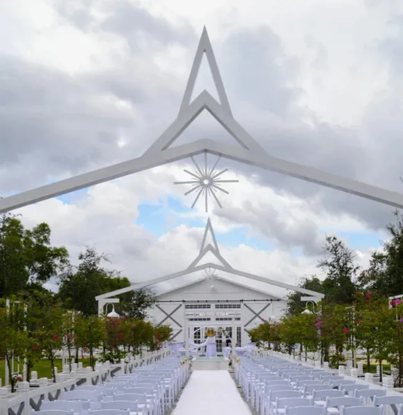 A white barn wedding venue with an outdoor ceremony aisle and chairs.