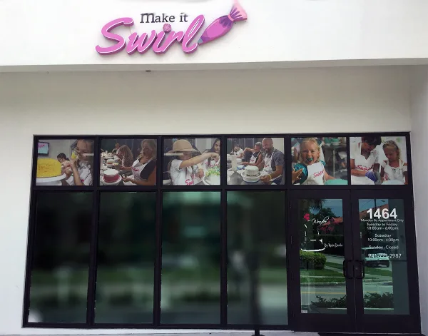 Exterior storefront of a cake shop with a 'Make it Swirl' sign and window displays showing people decorating cakes.