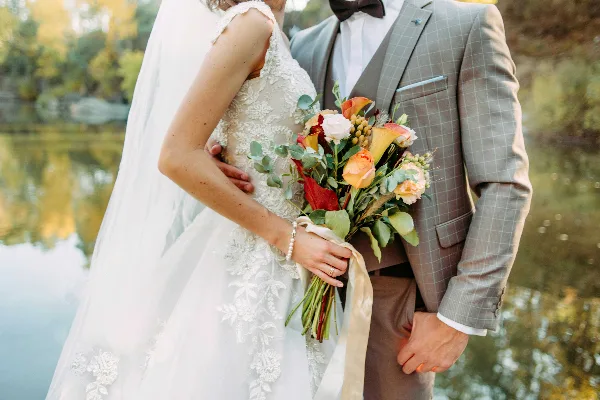 A bride and groom standing together outdoors, with the bride holding a bouquet of flowers.