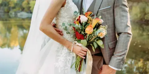 A bride and groom standing together outdoors, with the bride holding a bouquet of flowers.