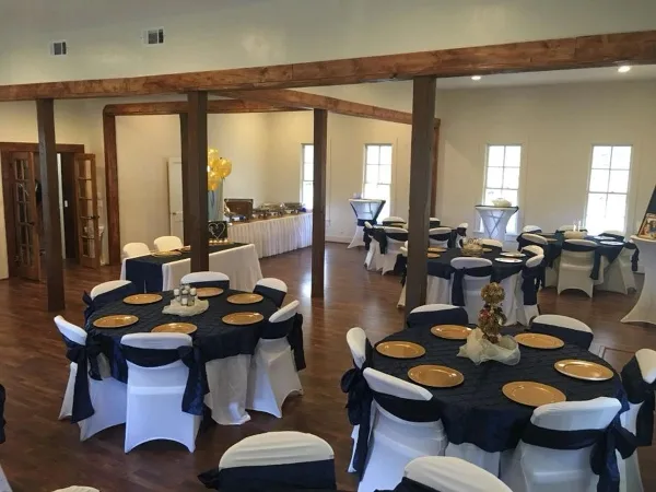 Interior view of a wedding reception hall with round tables, white chair covers, and wooden beams.