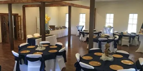 Interior view of a wedding reception hall with round tables, white chair covers, and wooden beams.