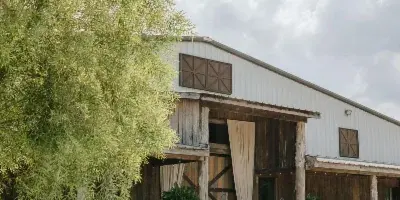 Exterior view of a rustic white and wood barn venue with a gravel driveway and landscaping.