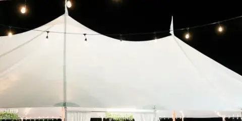 A large white event tent set up at night with string lights, containing tables and chairs for a wedding reception.