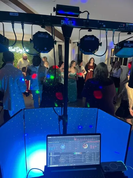 A DJ setup featuring a laptop, audio mixer, and a truss of Chauvet lighting fixtures at a wedding reception.