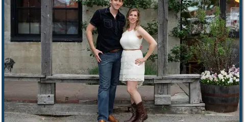 A man and a woman standing together in front of a rustic building, representing the Maine Music Makers band.