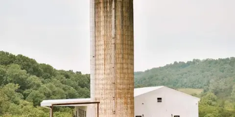 Exterior view of the Anderson Ridge event venue, showing a tall metal silo and a white barn building surrounded by green hills.