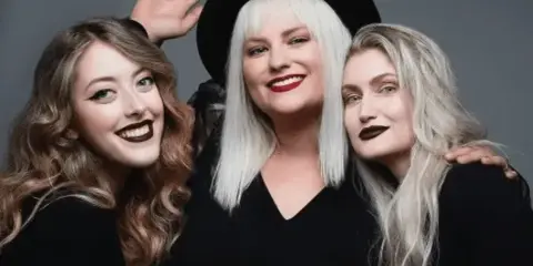 Three women posing together in a studio setting, showcasing professional hair styling and makeup.
