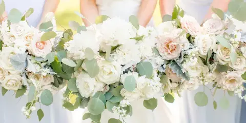 Close-up of a white and blush floral arrangement with eucalyptus held by bridesmaids.