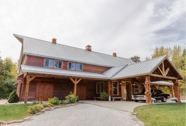 Exterior view of a large rustic wooden venue building with a metal roof and covered porch area.