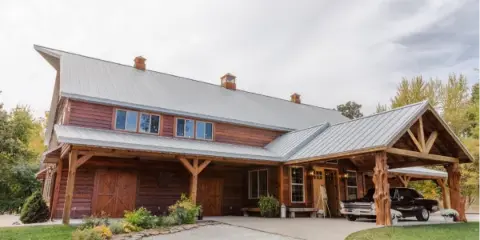 Exterior view of a large rustic wooden venue building with a metal roof and covered porch area.