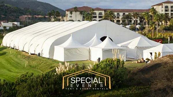 Large white event tents and structures set up on a grassy field with a resort building in the background.