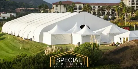Large white event tents and structures set up on a grassy field with a resort building in the background.