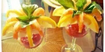 A close-up of a shrimp cocktail appetizer garnished with fruit and mint leaves.