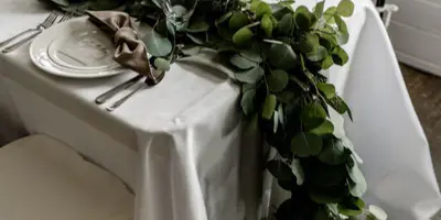 A wedding table setting featuring a white tablecloth, black chiavari chairs, and a long eucalyptus greenery runner.