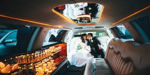 Interior view of a luxury limousine with a bride and groom seated in the back.