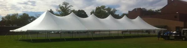 A large white multi-peak event tent set up on a green lawn with a brick building in the background.