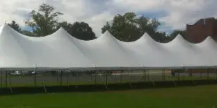 A large white multi-peak event tent set up on a green lawn with a brick building in the background.