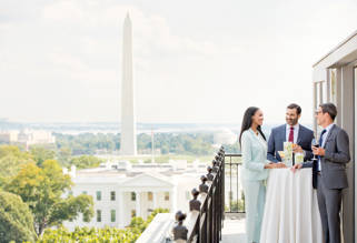 A wedding couple and officiant standing on a balcony with a view of the Washington Monument and the White House.