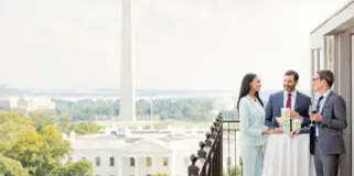 A wedding couple and officiant standing on a balcony with a view of the Washington Monument and the White House.