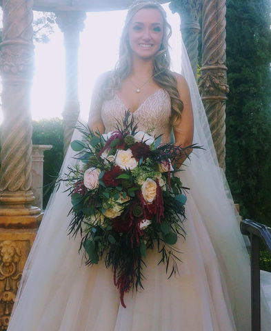 A bride in a white wedding dress holding a large, cascading bouquet of white and burgundy flowers with greenery.