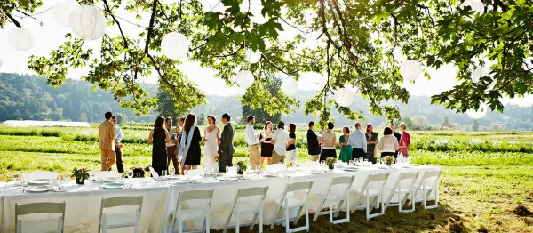 An outdoor event setup with long white tables and chairs arranged in a grassy field.