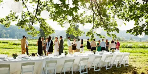 An outdoor event setup with long white tables and chairs arranged in a grassy field.