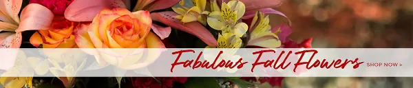 A close-up photograph of a vibrant floral arrangement featuring orange roses, pink lilies, and yellow alstroemeria.