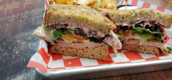 A close-up of a toasted sandwich cut in half, served on a metal tray with red and white checkered paper, accompanied by a side of chips.