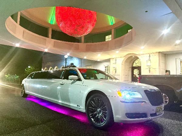 A white stretch limousine parked at a venue entrance with purple underglow lighting.