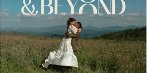 A bride and groom embracing in a grassy field with mountains in the background, with the text '& BEYOND' overlaid at the top.